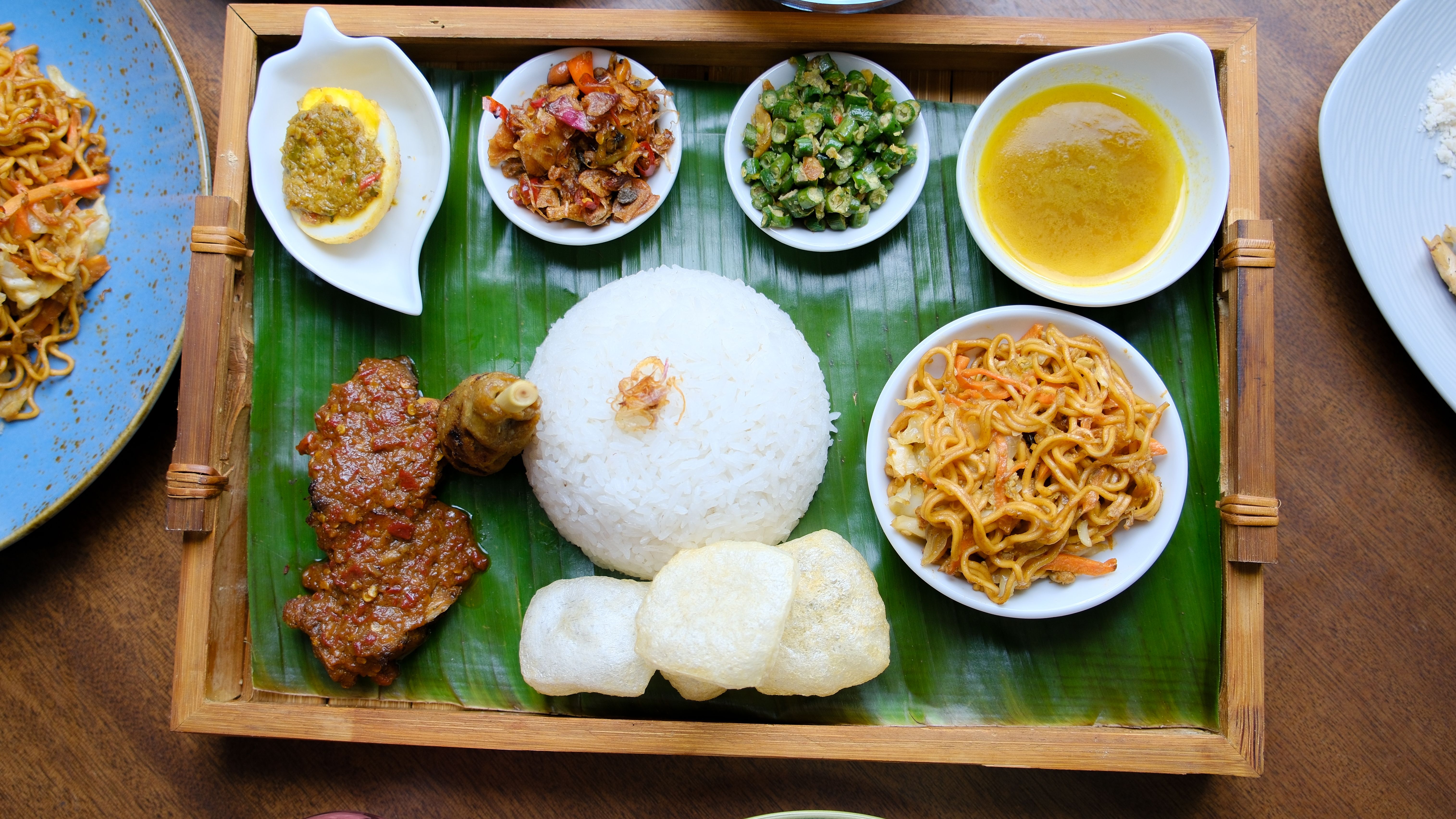 A colorful Indonesian meal featuring rice and traditional sides served on banana leaves.
