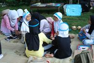 A group of children sitting on a mat outdoors engaged in a group activity wearing headbands.