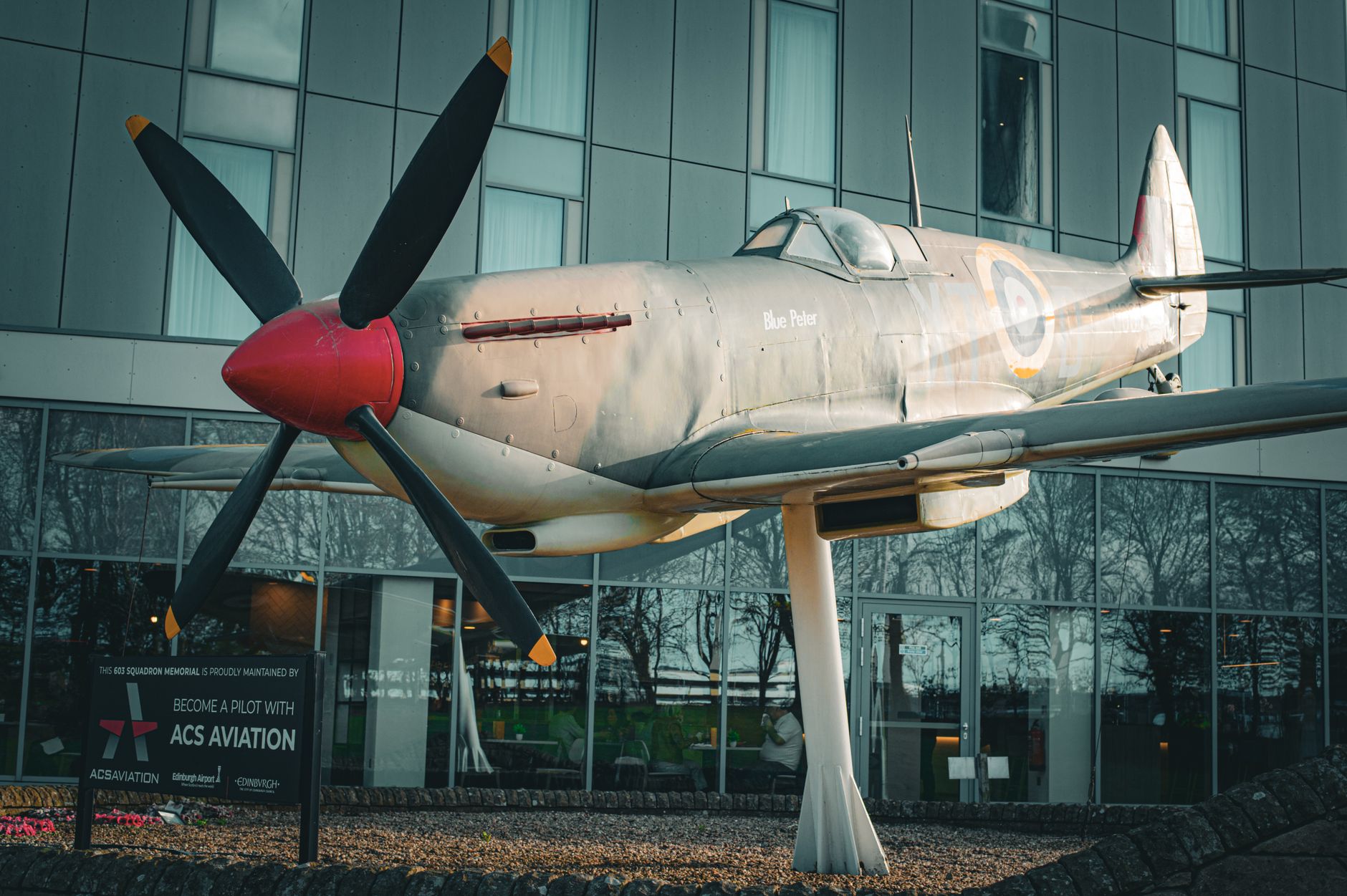 Replica of Spitfire aircraft displayed outside a museum building.