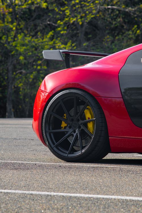 Free Close-up of a red sports car with custom black alloy wheel and yellow brake caliper in a parking lot. Stock Photo