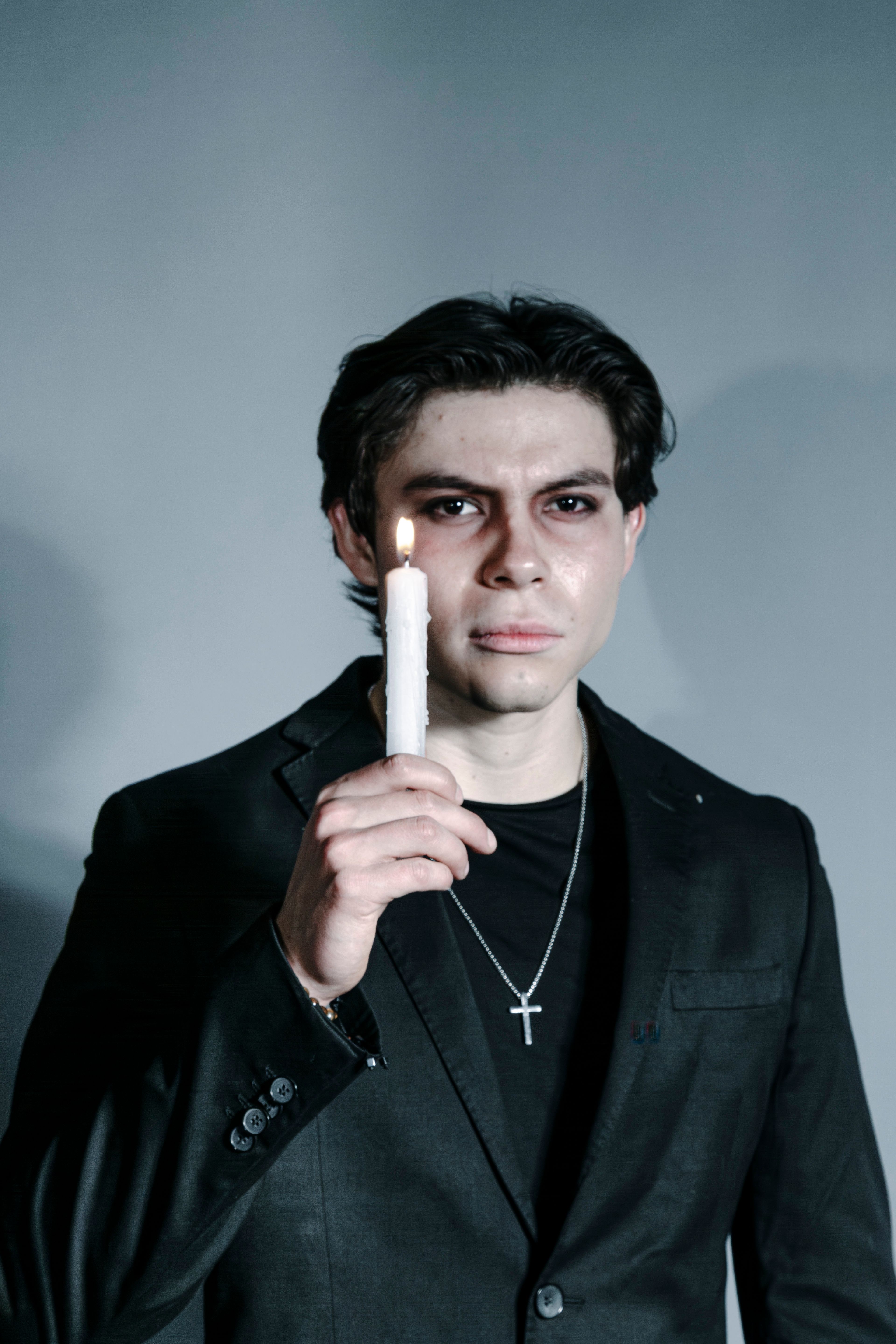 A young man in a dark suit holding a lit candle against a gray background.
