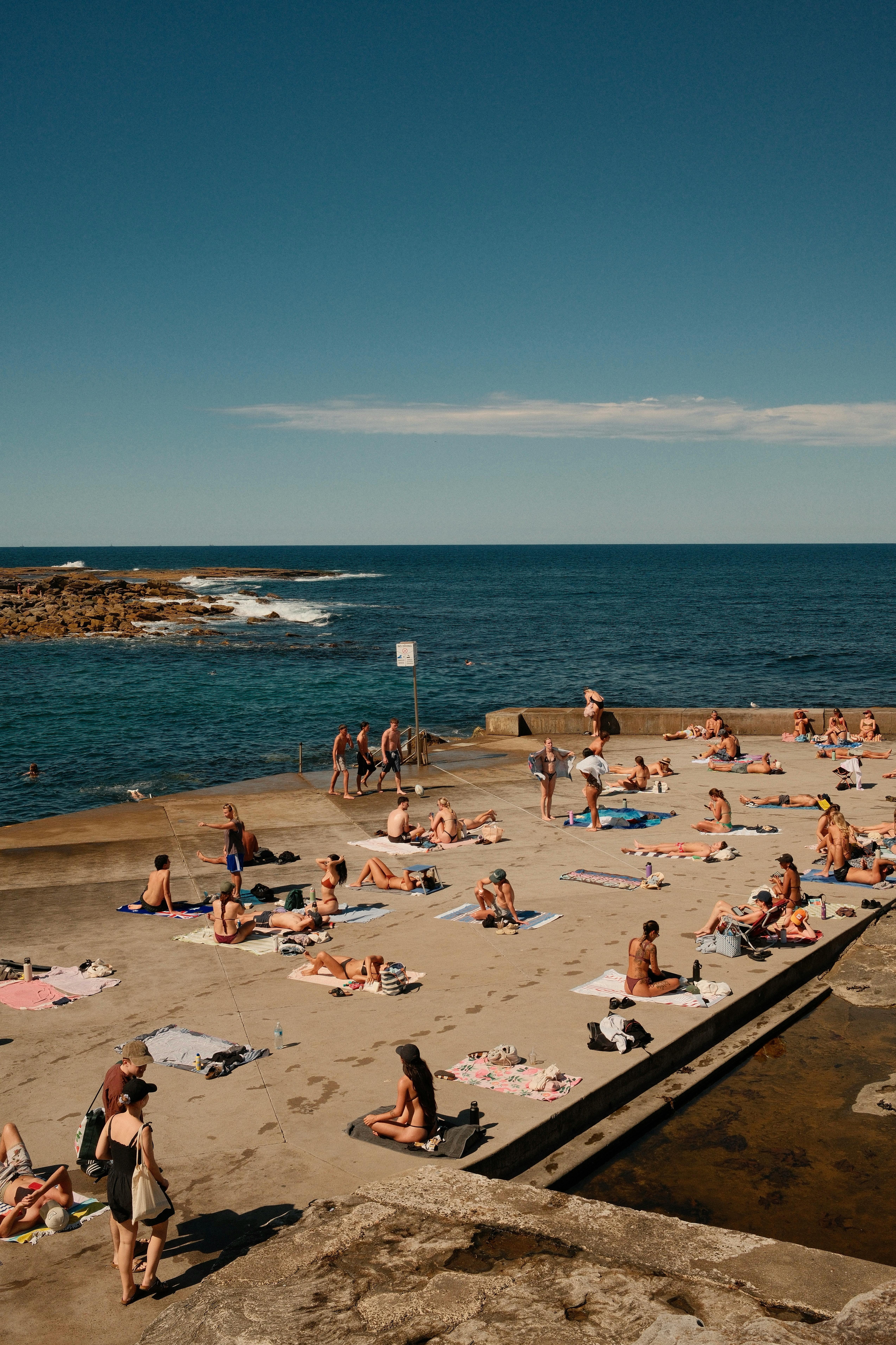 A bustling summer day on a Sydney beach with sunbathers by the ocean.