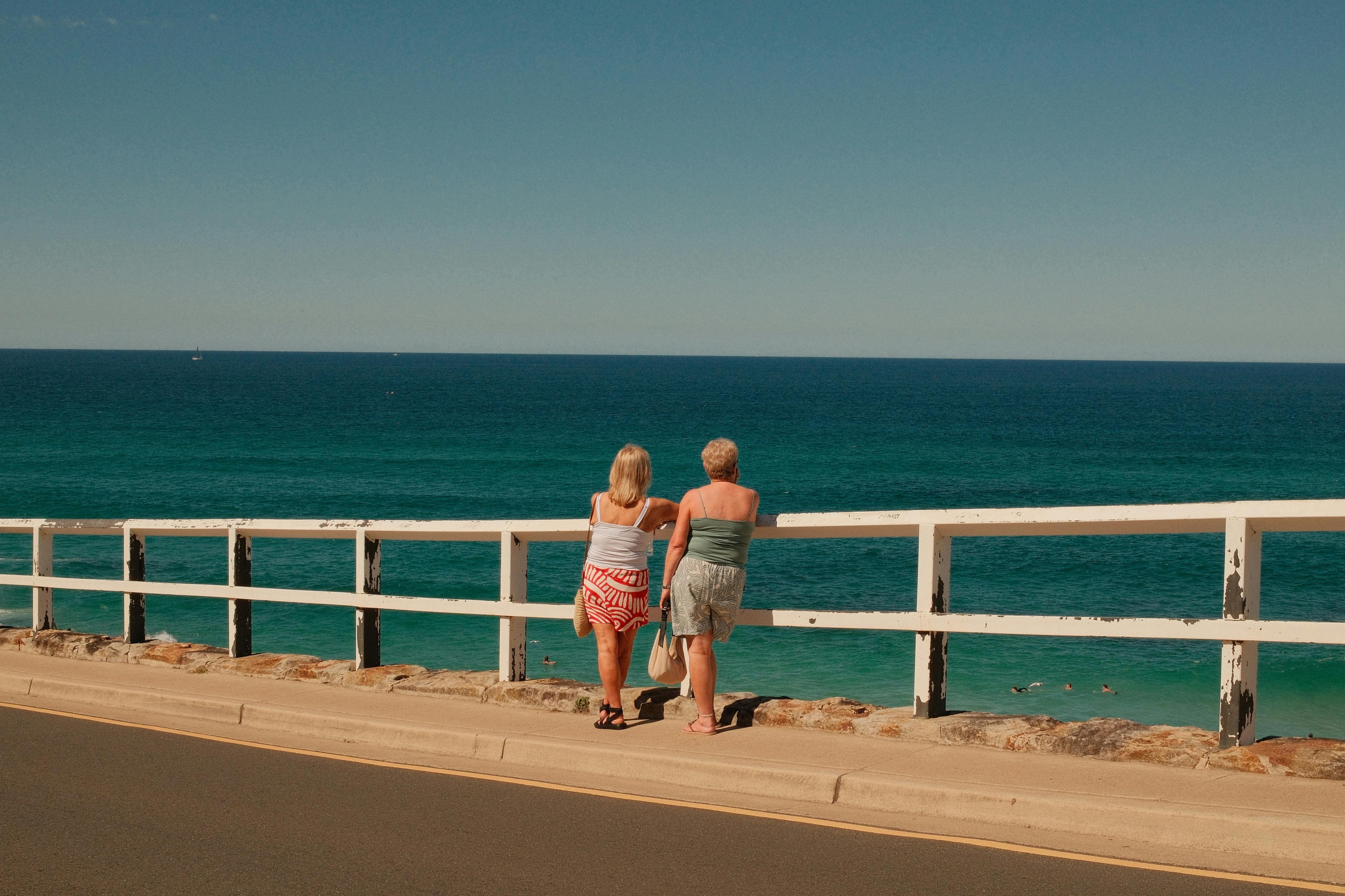 Two women admire the scenic coastline in Sydney, Australia, under a clear blue sky.