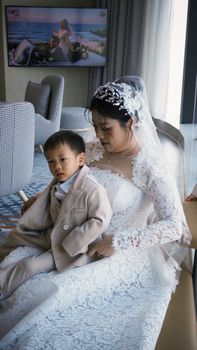 A Vietnamese bride in a lace gown with a young child at a wedding ceremony indoors.