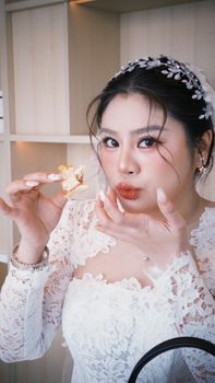 A beautiful Vietnamese bride in lace attire enjoys a piece of wedding cake indoors.