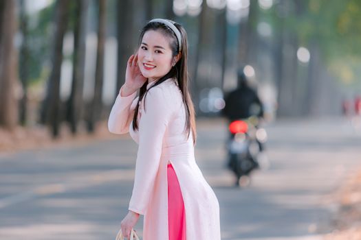 A woman in a pink traditional dress smiling on a tree-lined road in daytime.