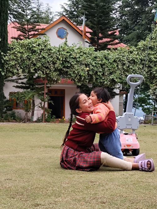 Free A joyful mother and child embrace on the grass in front of a scenic house surrounded by greenery. Stock Photo