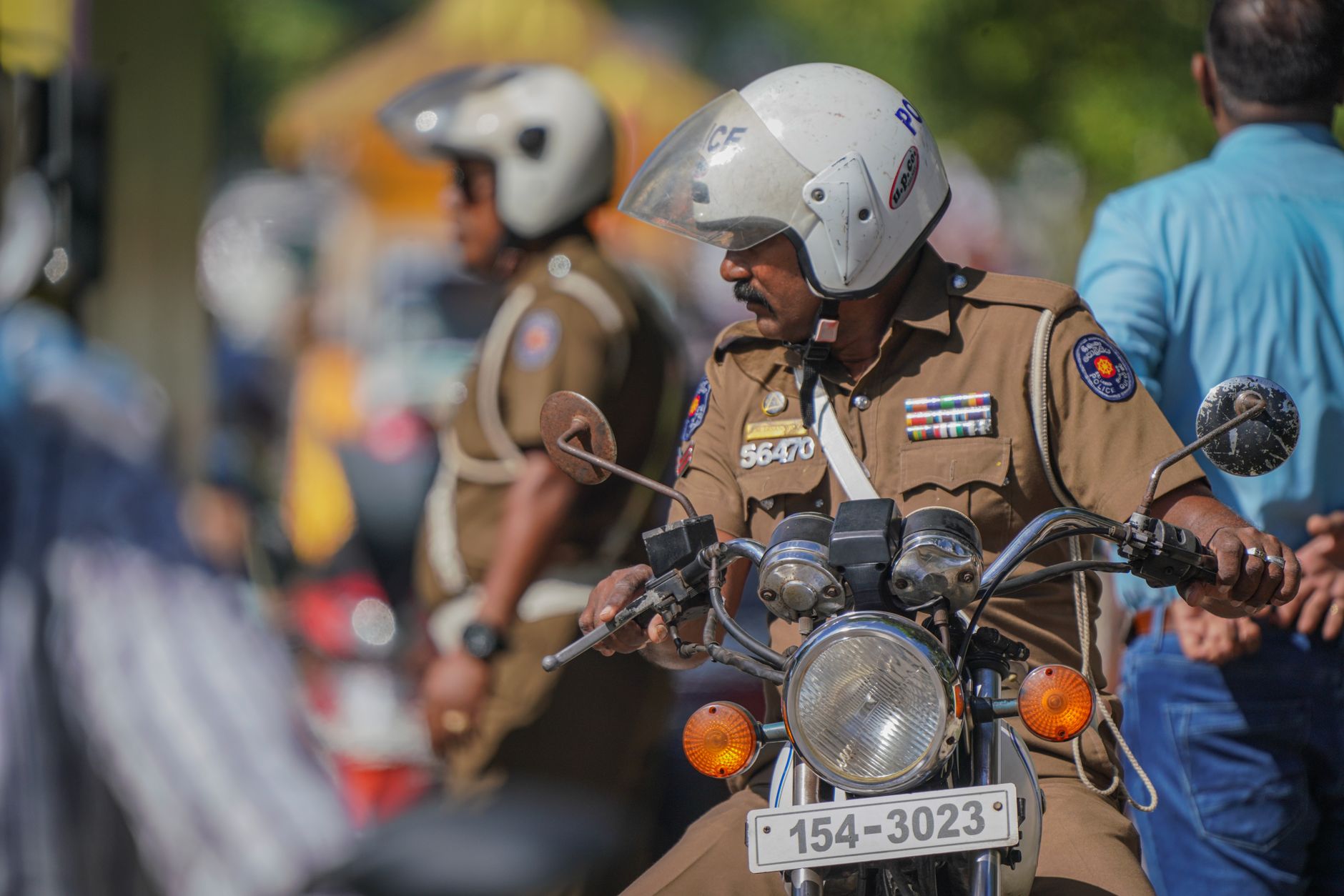 Close-up of a police officer riding a motorcycle during the day in a bustling urban environment.