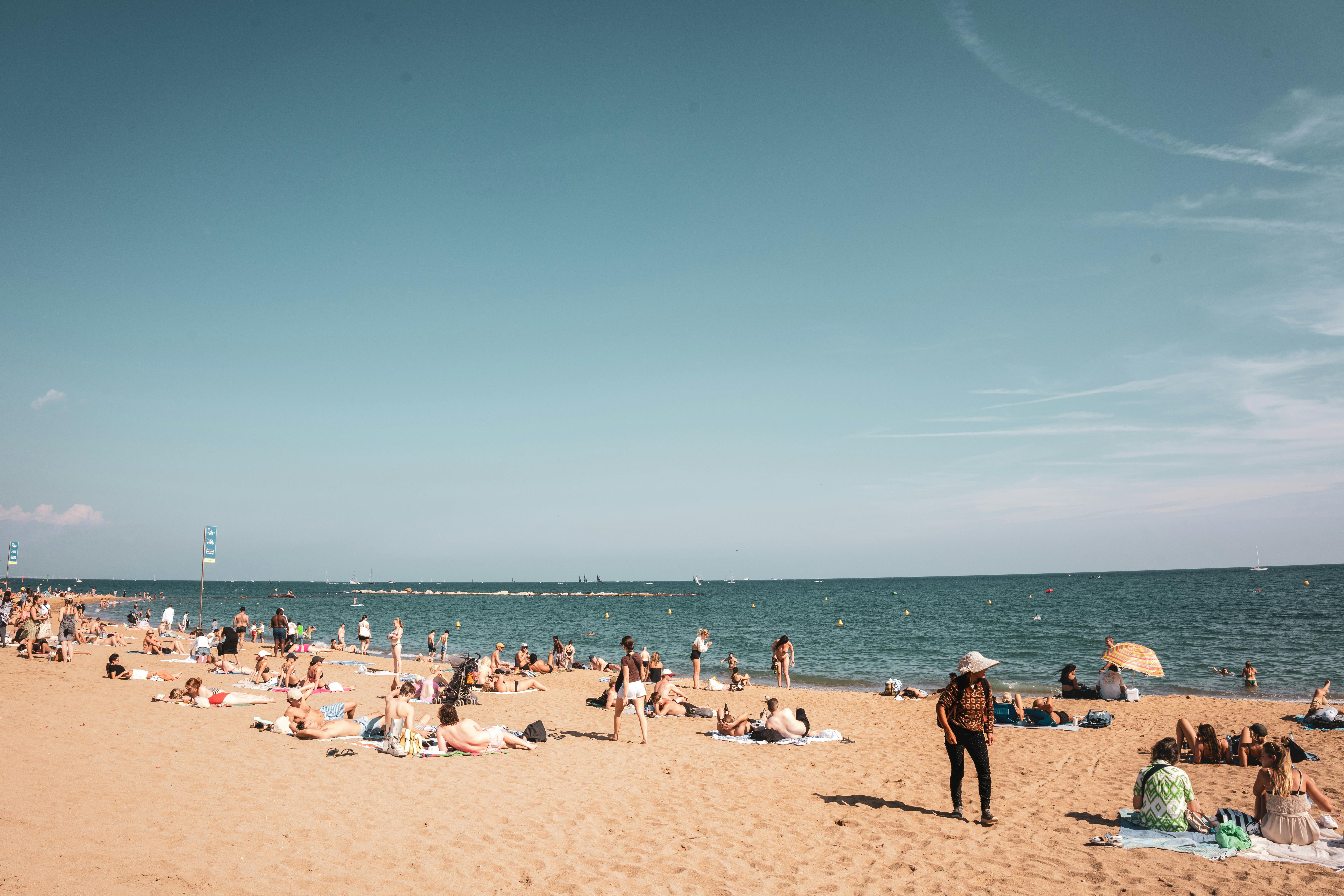 A vibrant sunny day at a Barcelona beach with people enjoying the sand and sea under a clear sky.