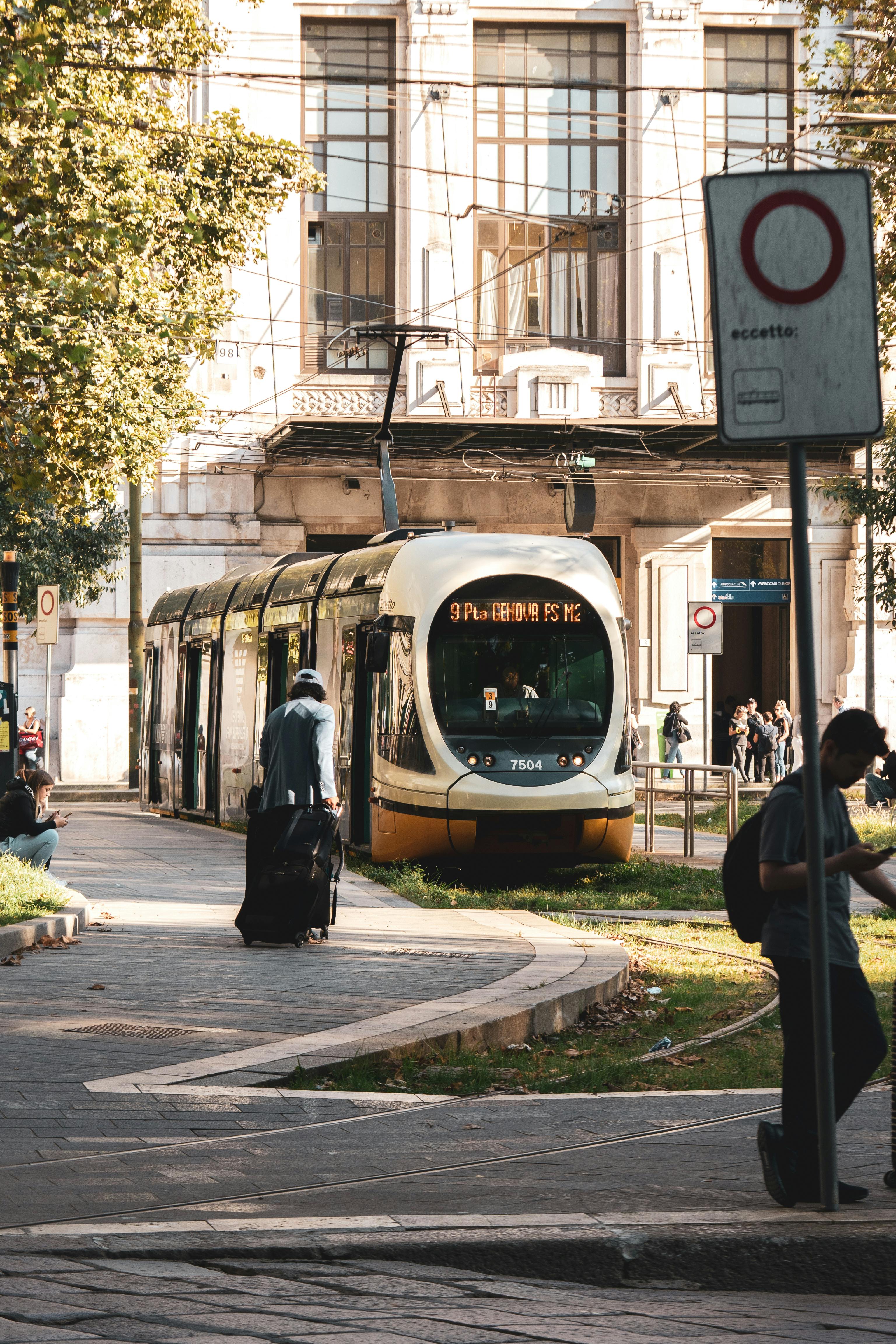 A modern tram stopped at a station in Milan, Italy, surrounded by people and urban architecture.