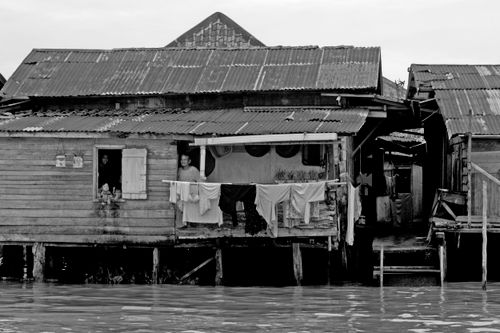 Free Black and white image of a rustic stilt house with people and drying laundry. Stock Photo
