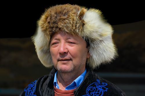 Free Man in a furry hat and embroidered coat, outdoors with a neutral background, showcasing traditional attire. Stock Photo