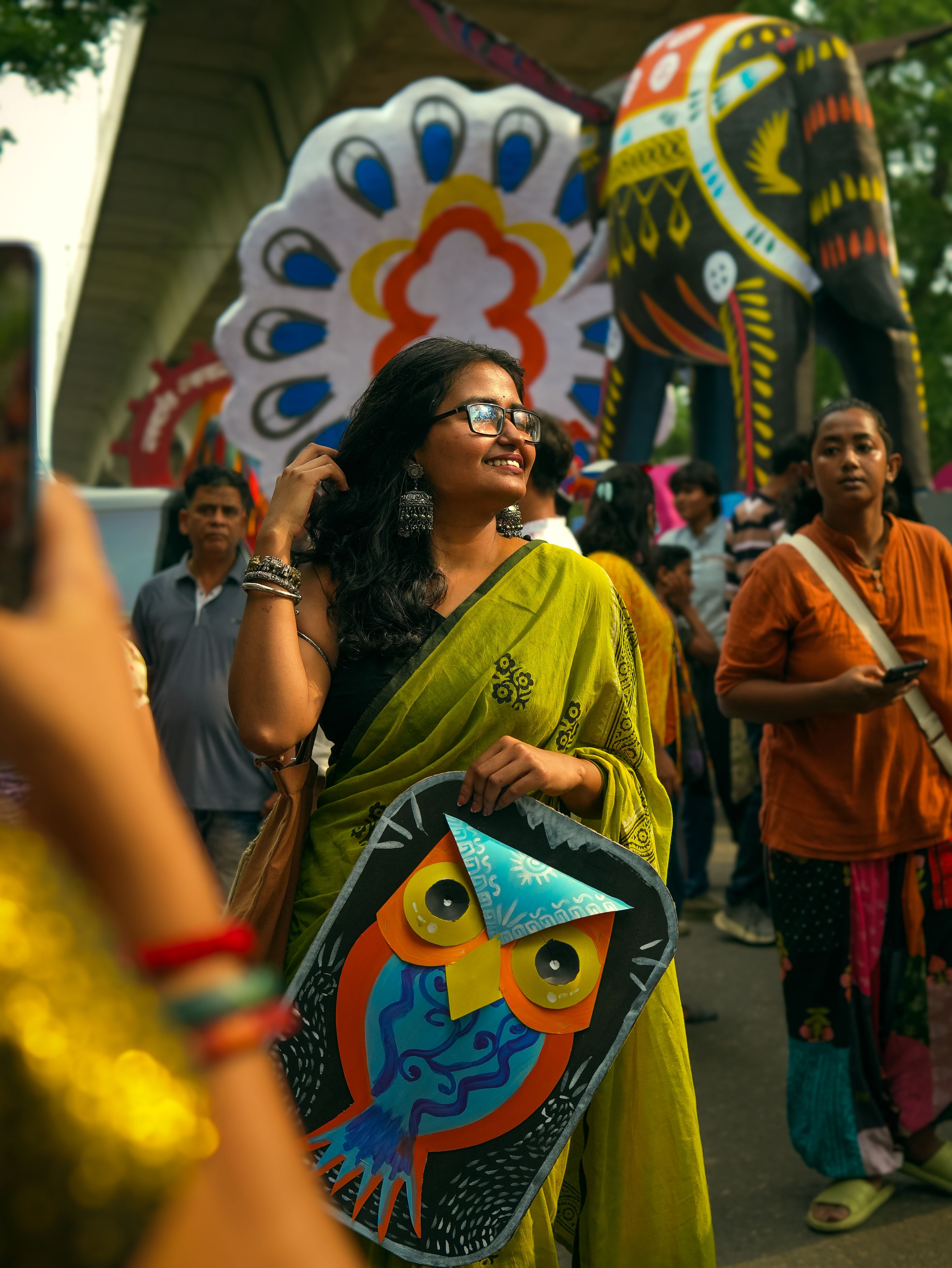 Vibrant festival scene with a woman in a sari holding colorful owl art.