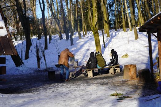 Group of people around a campfire in snowy Lublin forest during wintertime.