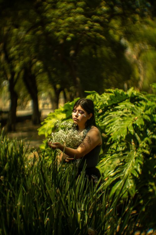 Free A woman with artistic makeup and bouquet stands in a lush park in Mexico City, embracing nature. Stock Photo