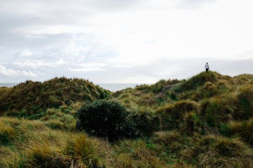 Free A serene view of a person walking through grassy hills with a cloudy sky above. Stock Photo