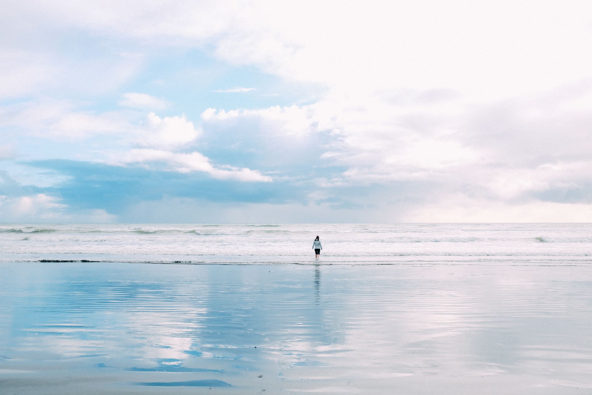 A solitary person stands by the ocean on a peaceful beach day.