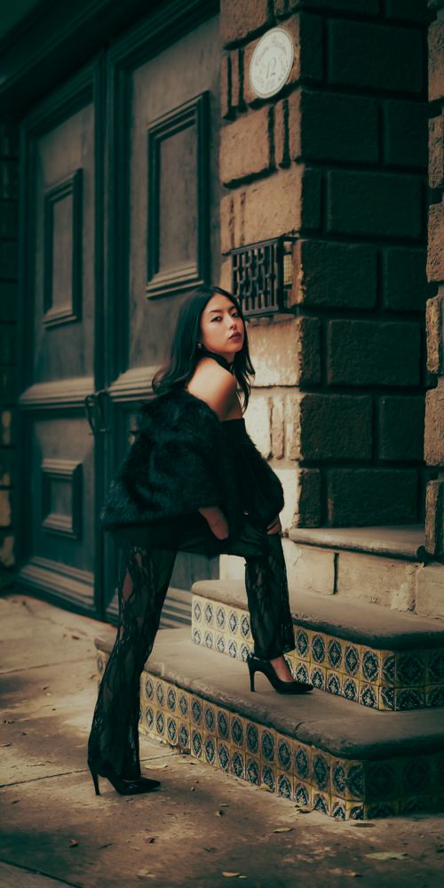 Free Stylish woman in a black outfit posing on decorated steps against an urban backdrop. Evening mood. Stock Photo