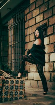 Stylish woman posing by a textured urban wall, conveying modernity and elegance.