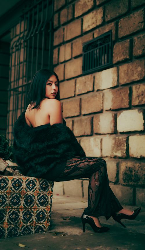 Free A stylish woman in lace and fur sits by a brick wall exuding elegance and allure. Stock Photo