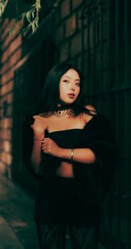 Elegant portrait of a young woman standing by a wall at night, exuding style and confidence.