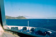 Through window of modern vessel floating on rippling sea against blue sky with rocky mountain in distance in coastal terrain