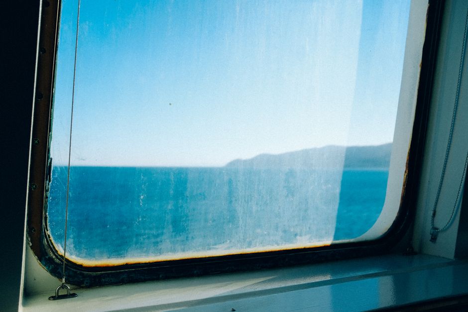 A tranquil ocean view through a slightly weathered ship window.