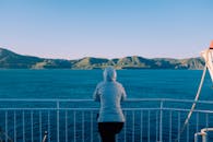 渡轮甲板上，一个穿着连帽衫的人正欣赏着大海和远处的岛屿