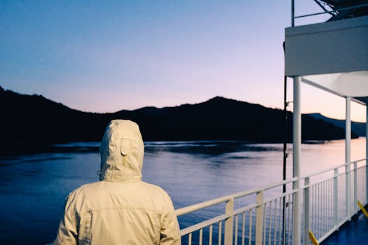 日落时分，一个穿夹克的人在渡轮甲板上凝望着宁静的水面