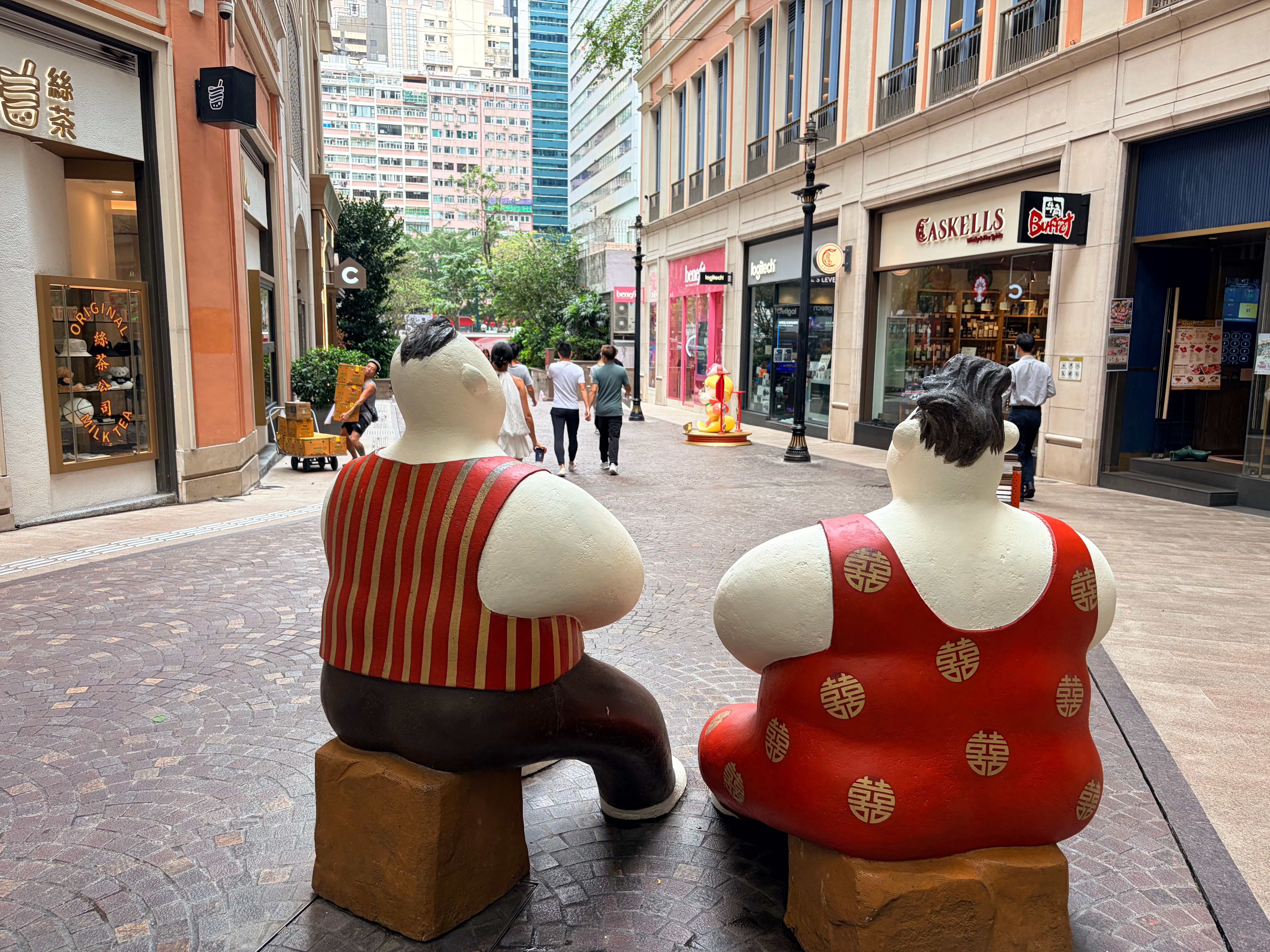 Colorful sculptures sit in a lively shopping street in Hong Kong, surrounded by retail shops and passersby.