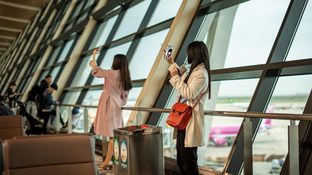 공항 터미널 창가에서 활주로를 바라보며 사진을 찍는 두 명의 한국인 여성 여행객