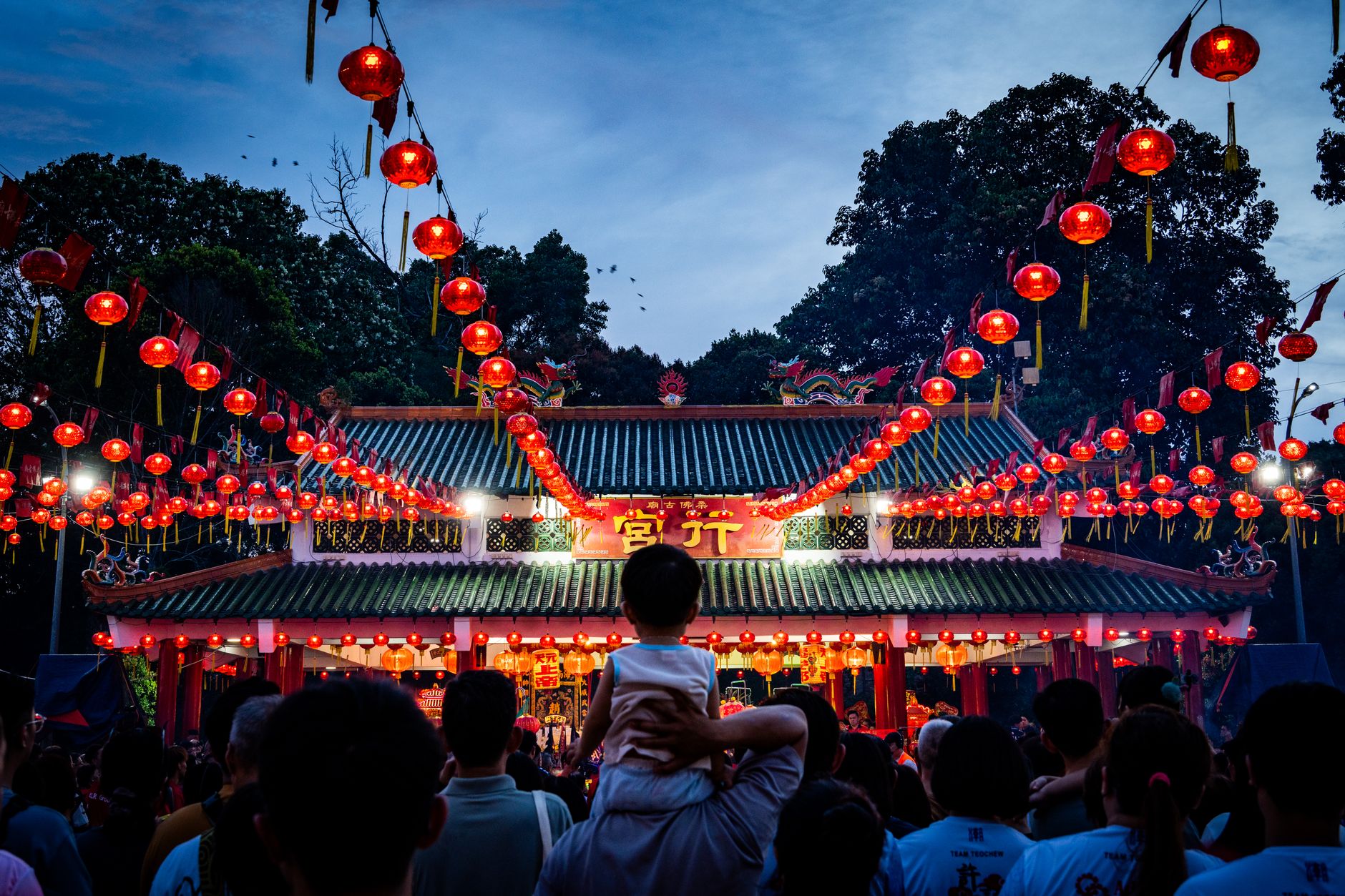 People gather at a brightly lit temple adorned with red lanterns during a cultural festival.