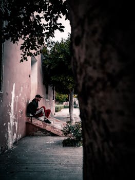 一名戴着帽子的男子若有所思地坐在城市小巷狭窄的室外混凝土台阶上