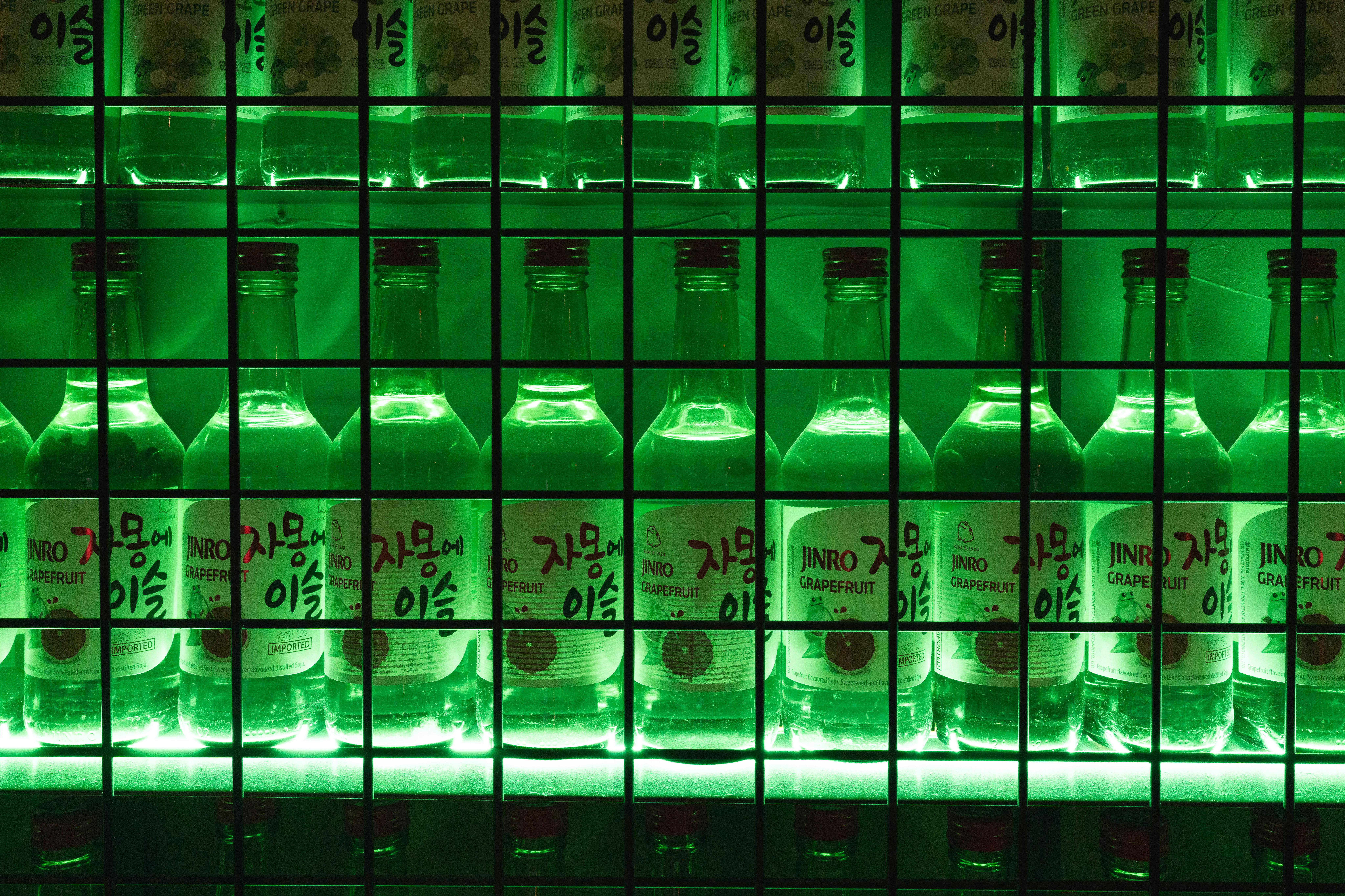 ingyenes Megvilágított Jinro grapefruit soju palackok egy élénkzöld fénnyel megvilágított polcon, merész és művészi látványt nyújtva. Stockfotó