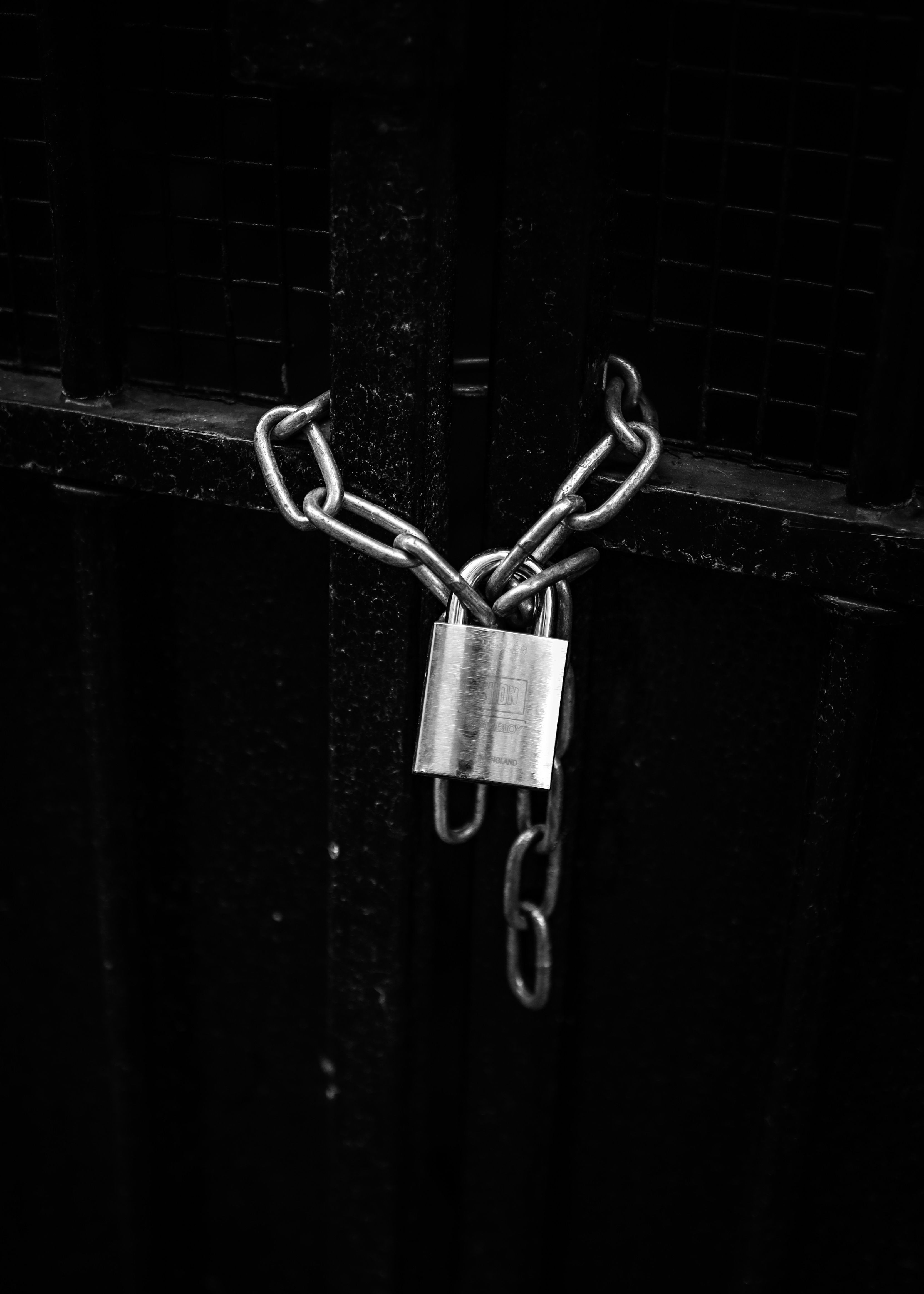 Black and white photo of a metal chain and lock securing a black gate, symbolizing security and protection.