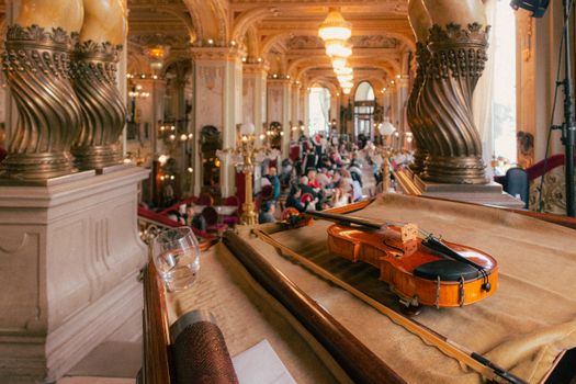 A violin rests elegantly in an opulent concert hall filled with people, exuding a classic musical ambiance.