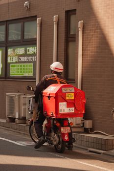Japanese postal worker delivering mail in Tokyo, Japan, on a red motorcycle. Urban city scene.