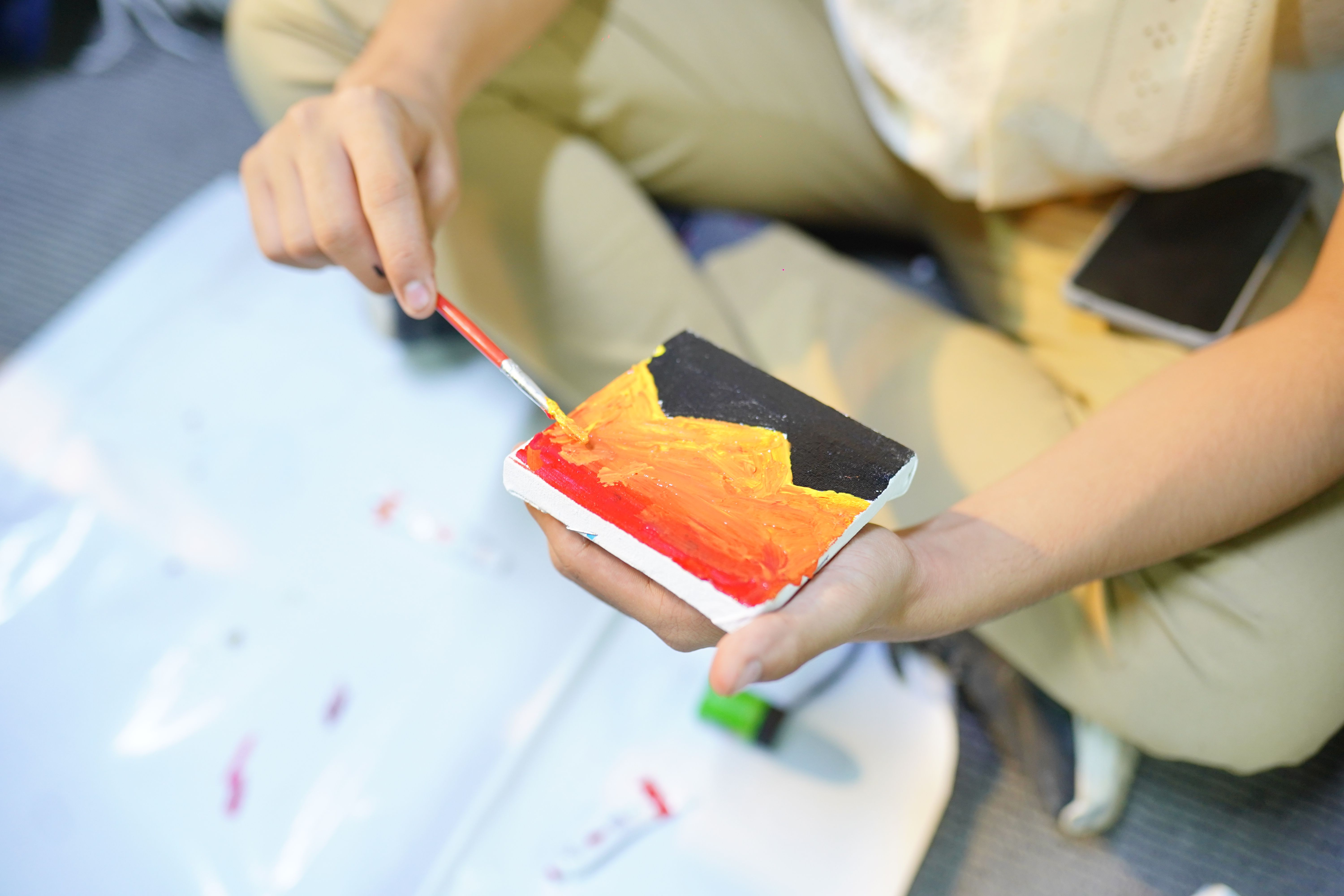 A person painting vibrant abstract art on a small canvas with red, orange, and black colors.