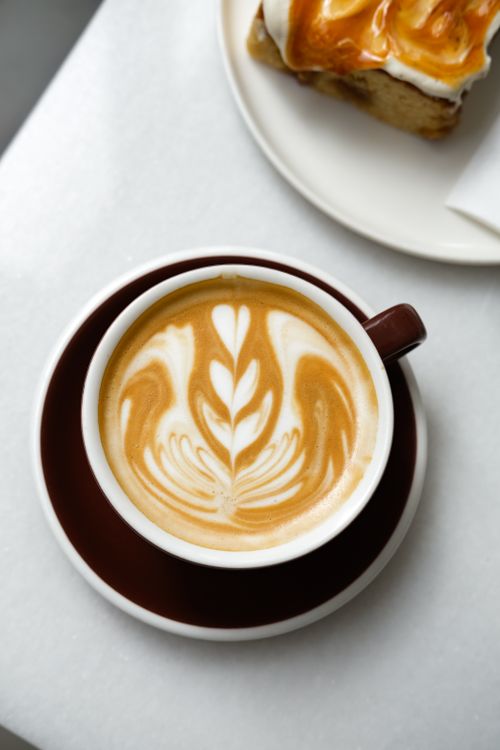 Free Top view of a beautifully crafted latte with latte art, accompanied by a sweet pastry on a white table. Stock Photo