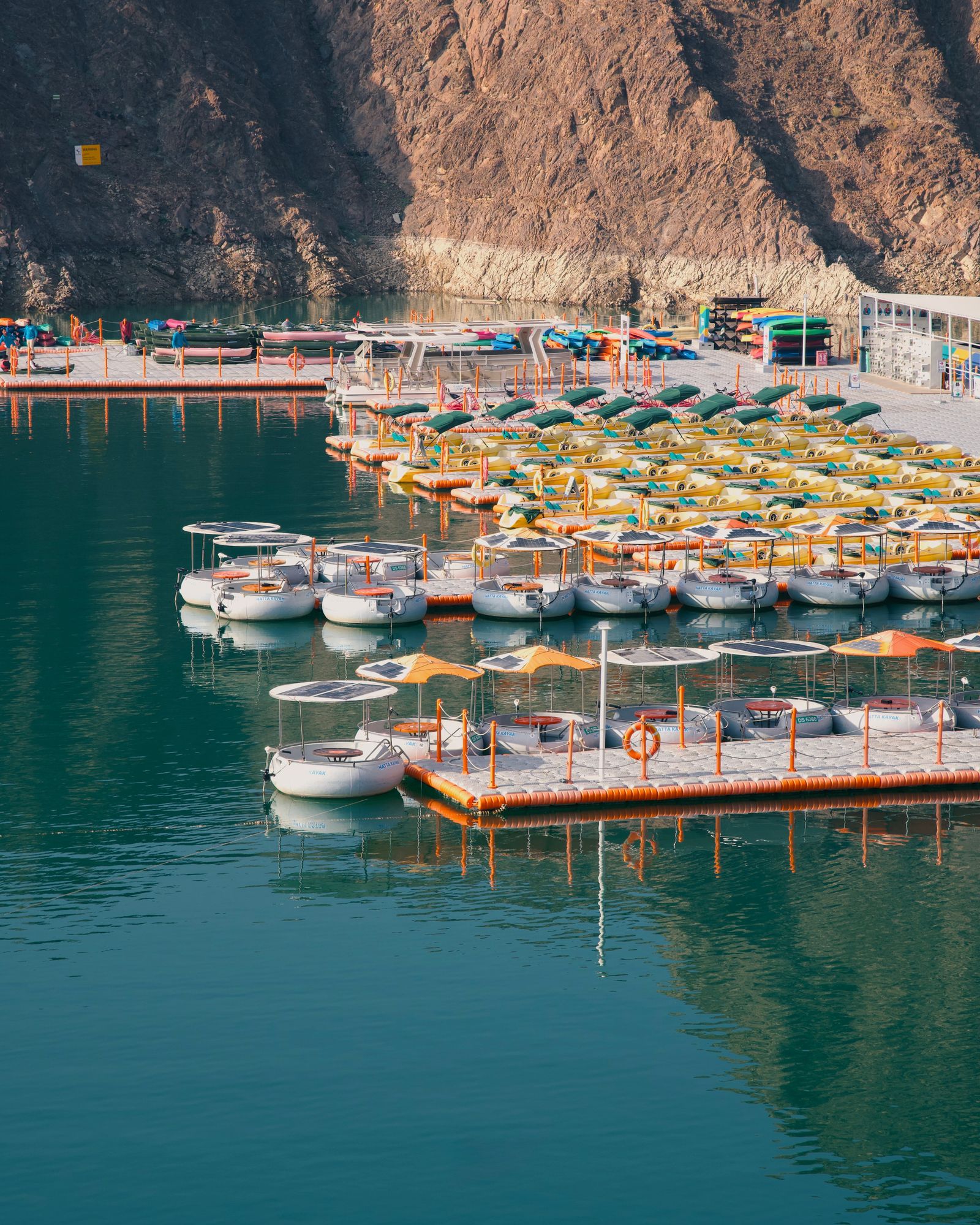 Pedal boats and kayaks moored on Hatta Dam, below the rocky Hajar Mountains