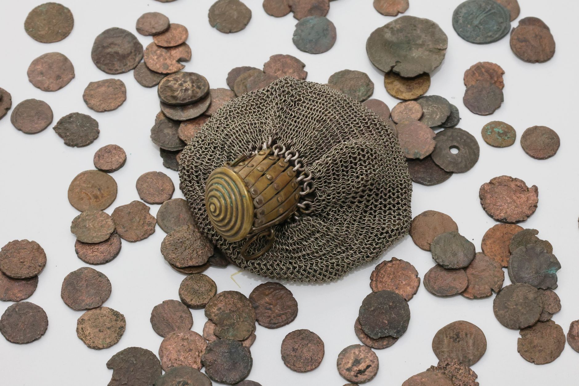Collection of antique coins surrounding an ornate chainmail glove on a clean white background.