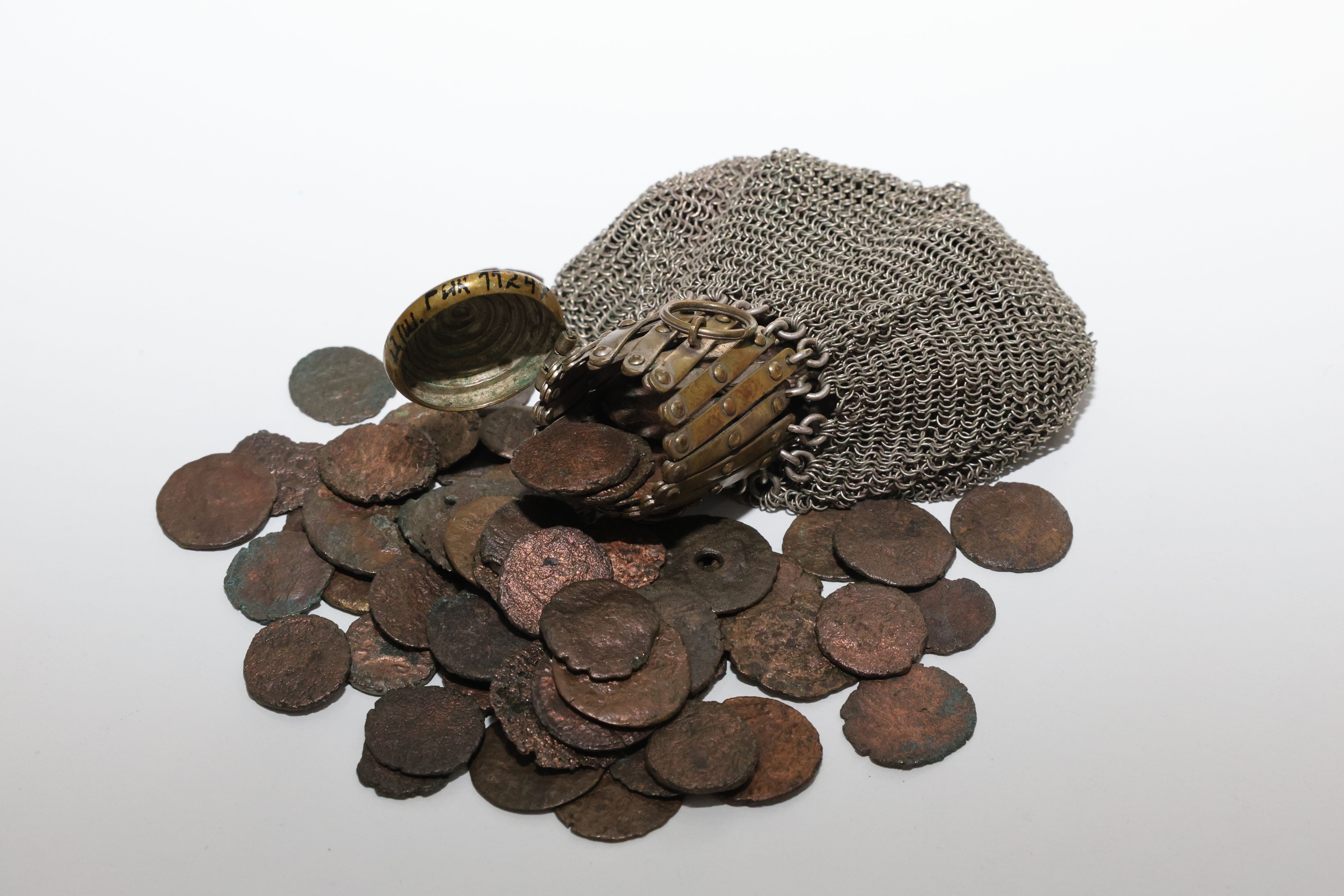 A collection of ancient coins spilling from a medieval chainmail coif, symbolizing history.