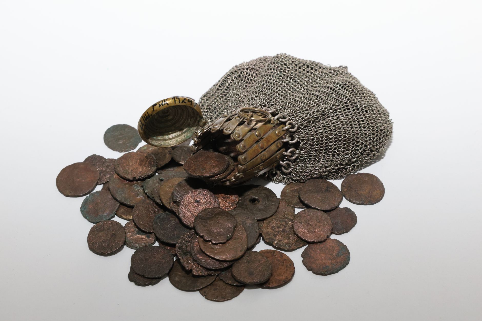 A collection of ancient coins spilling from a medieval chainmail coif, symbolizing history.