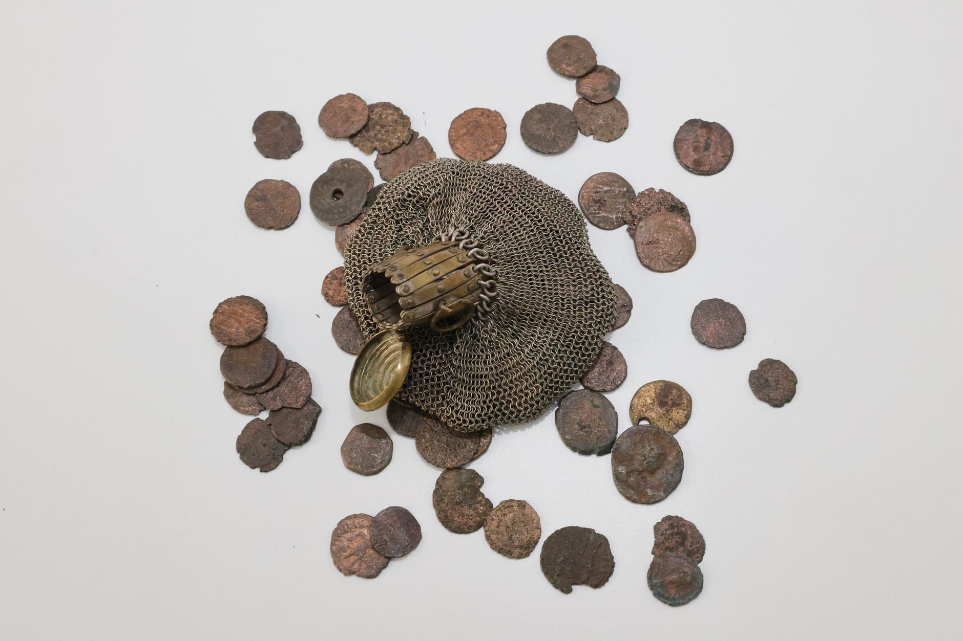 Top-down view of ancient coins scattered with a historical chainmail glove on a white surface.