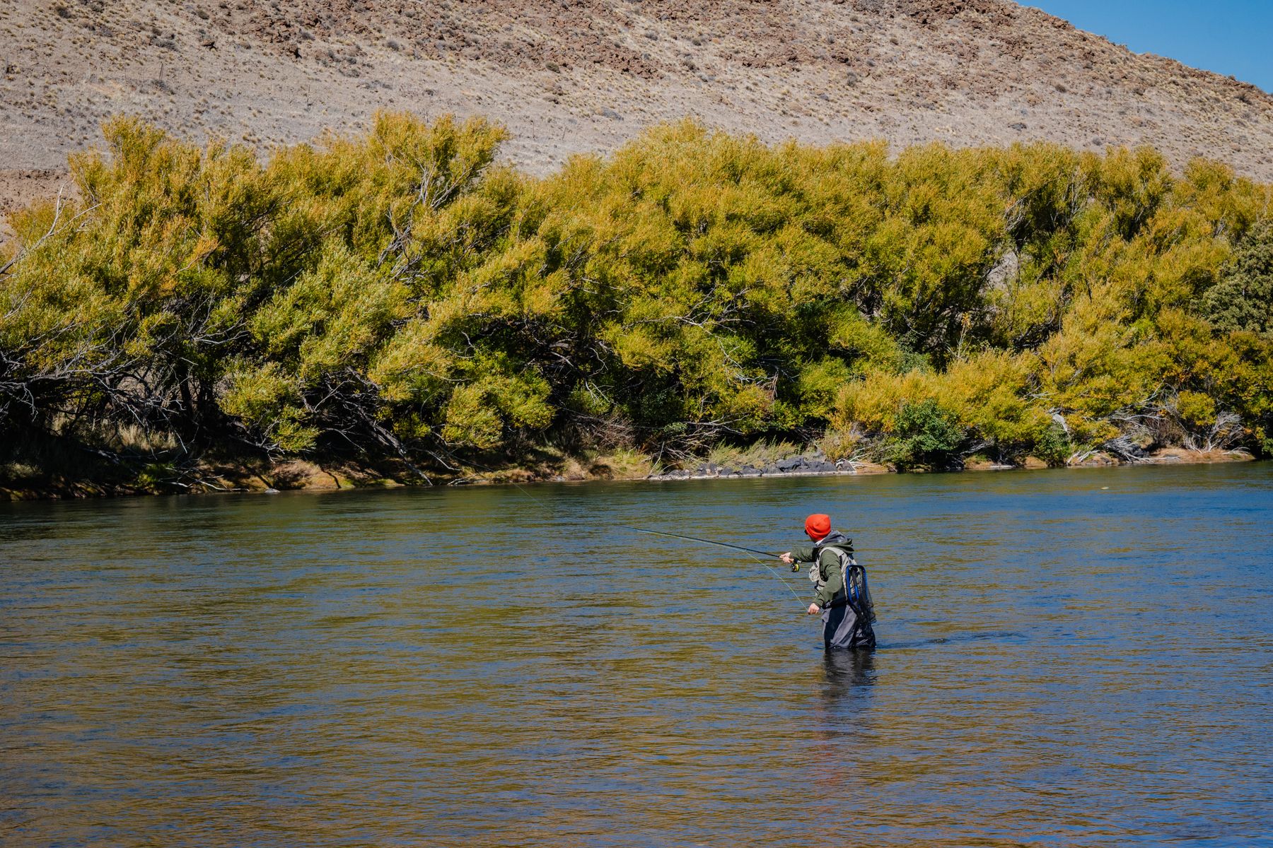 A person fly fishing in a serene river surrounded by autumnal trees
