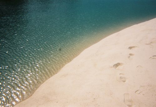 Free Footprints on sandy beach by calm blue waters evoke serenity and solitude. Stock Photo