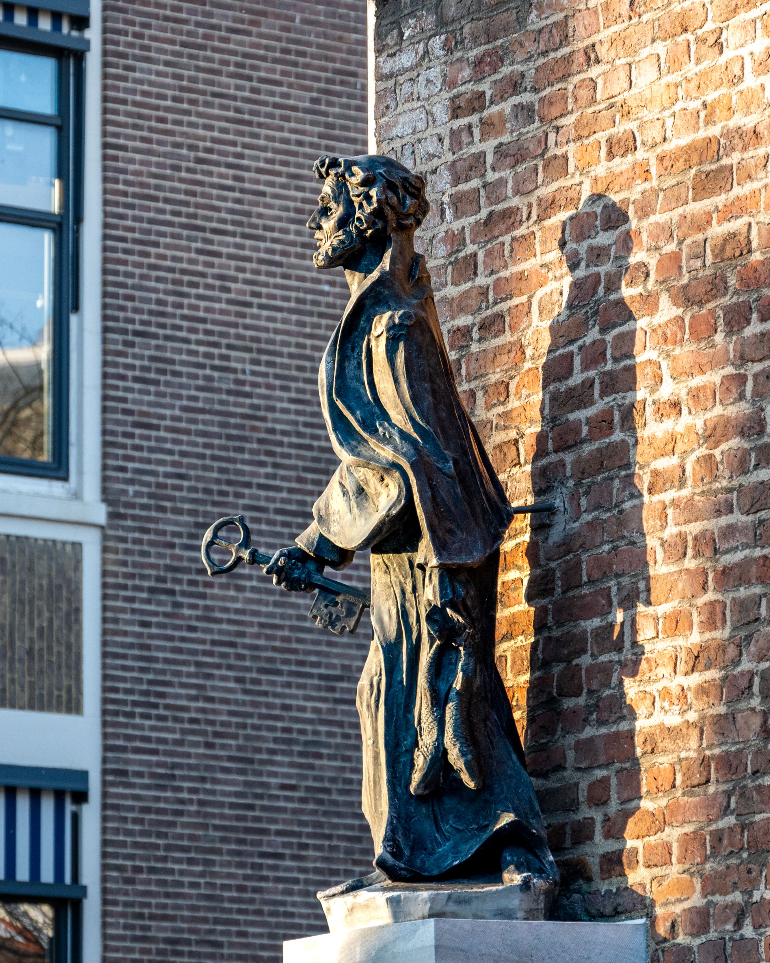 A bronze statue captured in sunlight against a historic brick wall in Sittard.