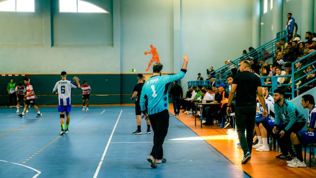 Dynamic handball match with players, referees, and spectators in a gymnasium.