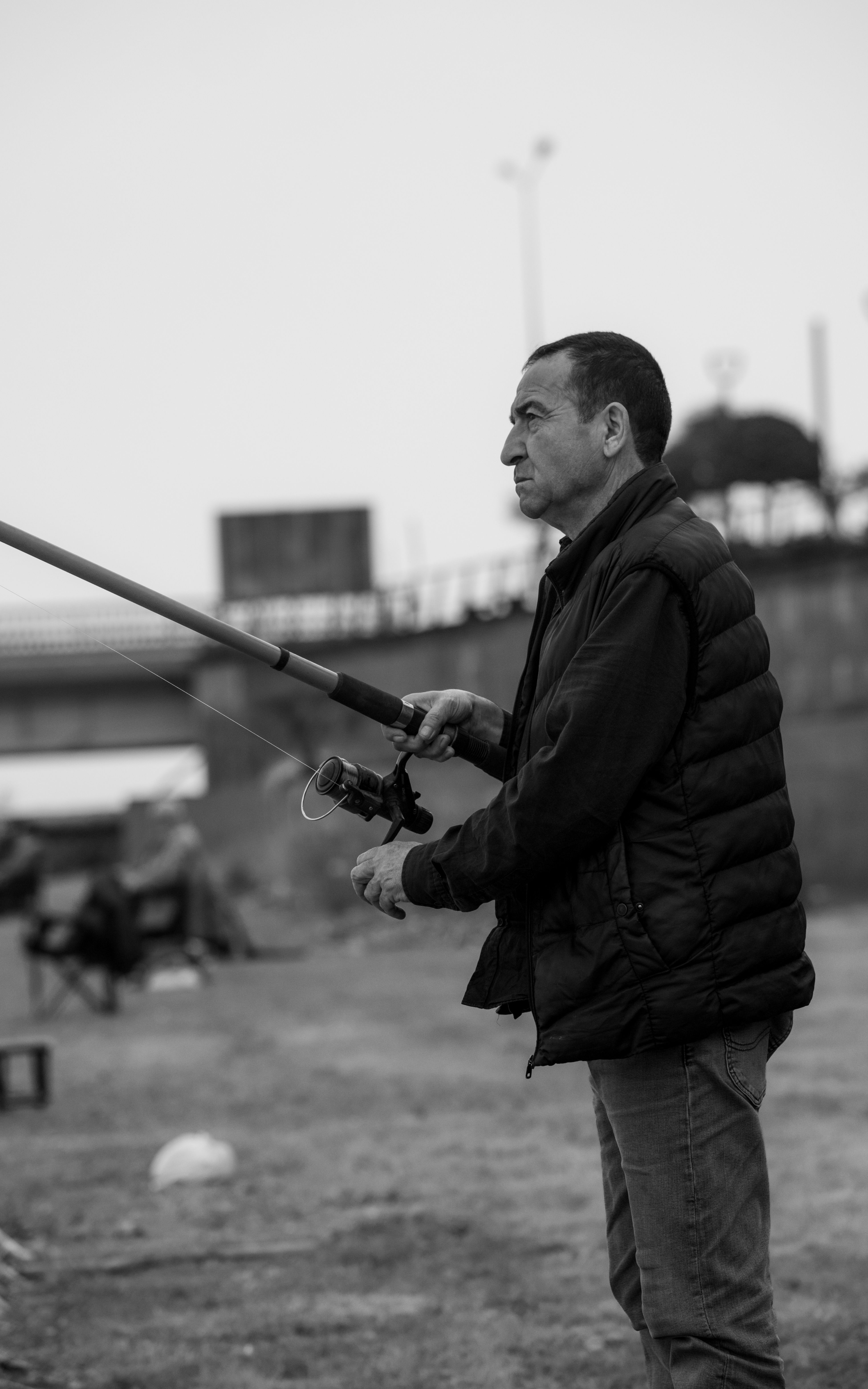A man engaged in fishing by a riverside in a serene black and white setting, conveying calmness.