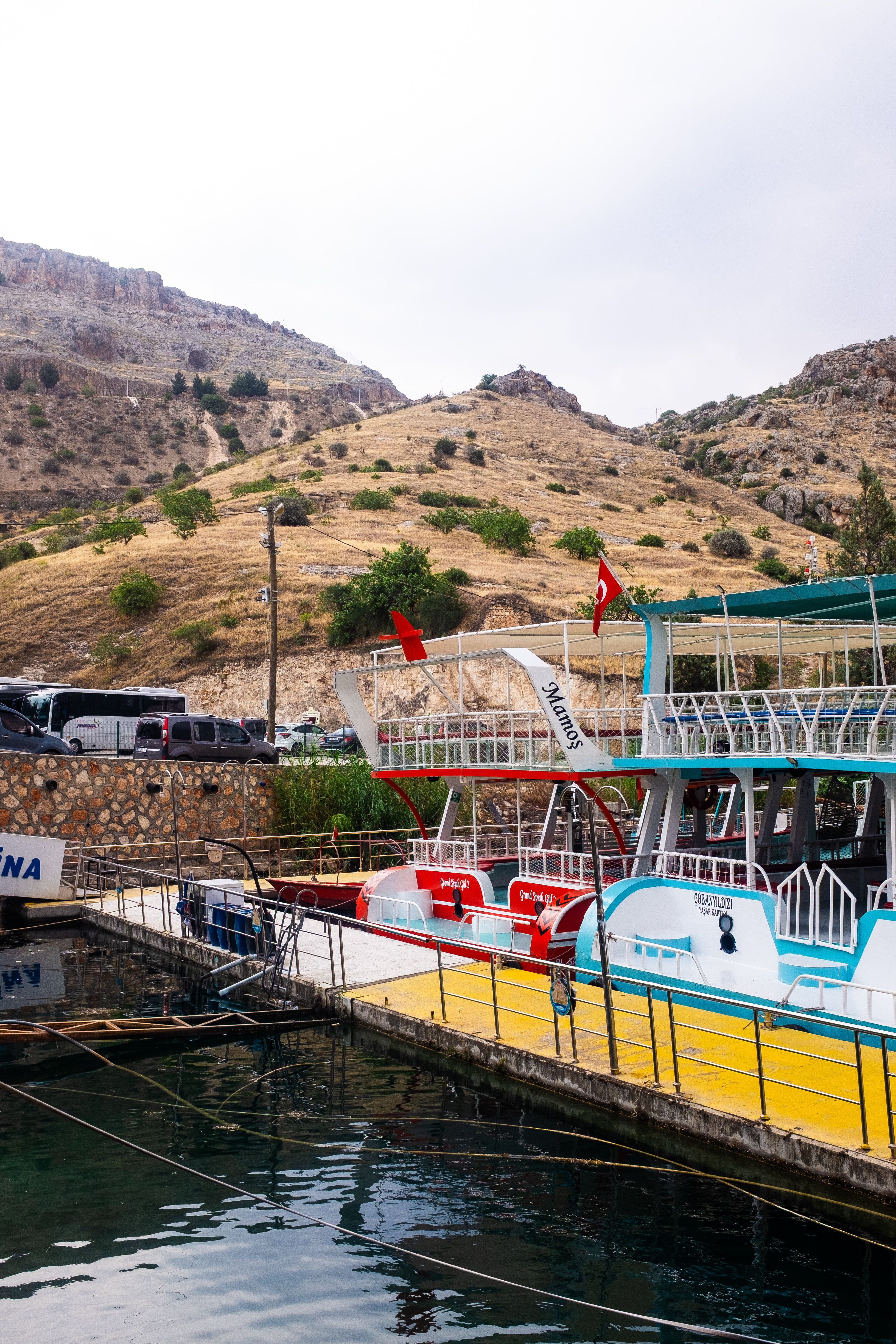 Tranquil harbor scene with boats docked at a pier below dry, rocky hills in a serene setting.
